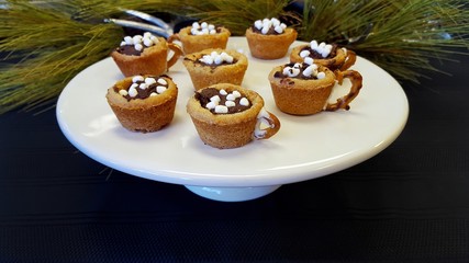 hot chocolate cookie cups on white pedestal plate with pine
