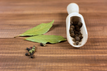 Allspice in wooden spoon, dry bay leaf and black pepper on brown background.