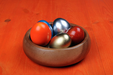 Easter composition. Colorful eggs in a wooden bowl on an orange wooden background. partially tinted photo.