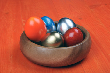 Easter composition. Colorful eggs in a wooden bowl on an orange wooden background. partially tinted photo.