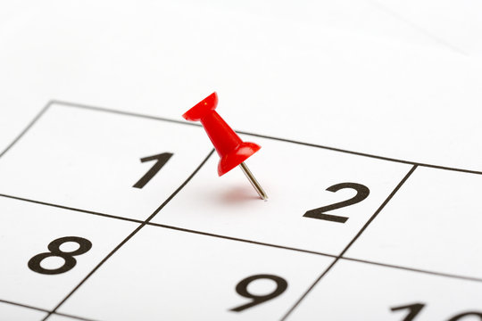 Pin on the date. The second day of the month is marked with a red thumbtack. Focus point on the red pin.