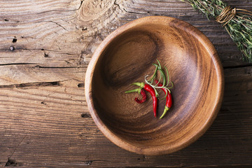 bowl made of wood with  simple wooden rustic background  red peppers and sharp beam thyme tied  cotton twine. View from above. Room for text