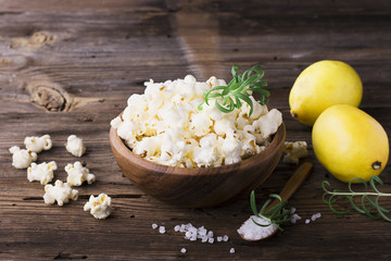 Salty crunchy fresh homemade popcorn flavored with lemon peel and rosemary scent in a wooden bowl on  simple  background. The concept of natural  organic seasonal food