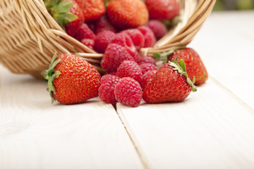 raspberry and strawberries in a basket on the table in garden