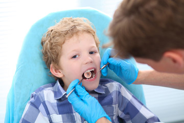 Little boy opening his mouth wide during inspection of oral cavity by dentist.