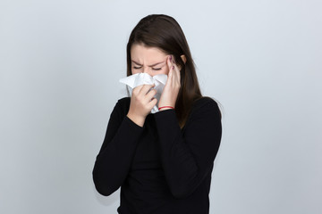 Portrait of a pretty woman in turtleneck sweaterand  having flu. girl blowing nose standing over gray background