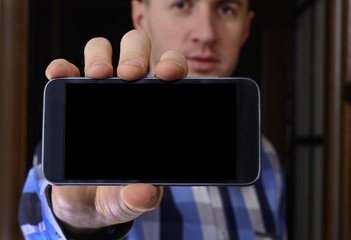 Young man in a checkered blue shirt is holding a phone with the 