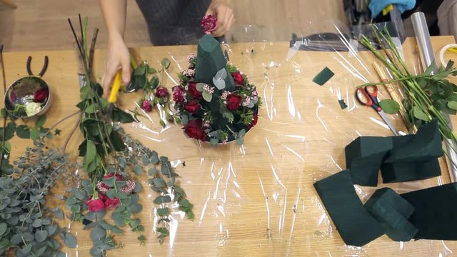 Florist decorates bouquet by pink roses with ruby color impregnations.