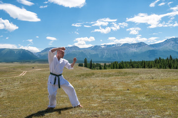 Fototapeta na wymiar Man in white kimono and black belt training karate on mountain background.