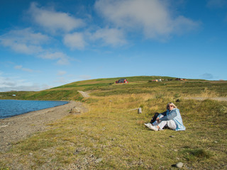 Fototapeta na wymiar Senior woman is sitting on the grass at Vatnsnes, Iceland