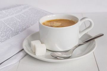 Morning composition with cup of  coffee with foam, two pieces of sugar and new papper on white wooden background