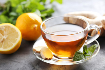 Cup of tea with ginger root and lemon on grey wooden table