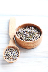 Lavender flowers in bowl and spoon on white wooden table