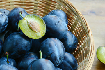 Many fresh Plums or Zwetschge and cut can see the seed in basket on wooden floor.