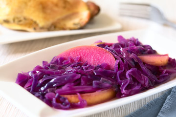 Geschmorter Rotkohl mit Apfel, Hähnchenschenkel im Hintergrund, fotografiert mit natürlichem Licht (Selektiver Fokus, Fokus in die Mitte des Bildes) © Ildi