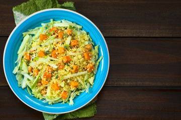 Salad of roasted pumpkin, green apple, couscous and iceberg lettuce seasoned with fresh thyme, photographed overhead on dark wood with natural light