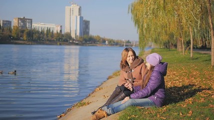 mother talking with her daughter on the promenade. Autumn sun's rays are reflected on the river. slow-motion - Powered by Adobe