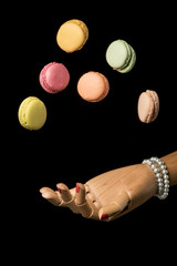 Hand of woman retrieves falling macaroons isolated on black background. Sweet and colorful candy. Vanilla, lemon, raspberry, strawberry, pistachio, rose, orange tastes macaroons. Dessert...