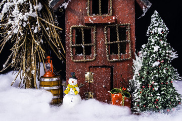 arts and crafts miniature scene of rustic house in deep snow with snowman, gifts, and Christmas tree