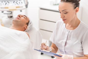 Fototapeta premium Professional cosmetologist making notes before procedure