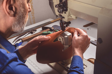 craftsman stitching a leather part of the shoe