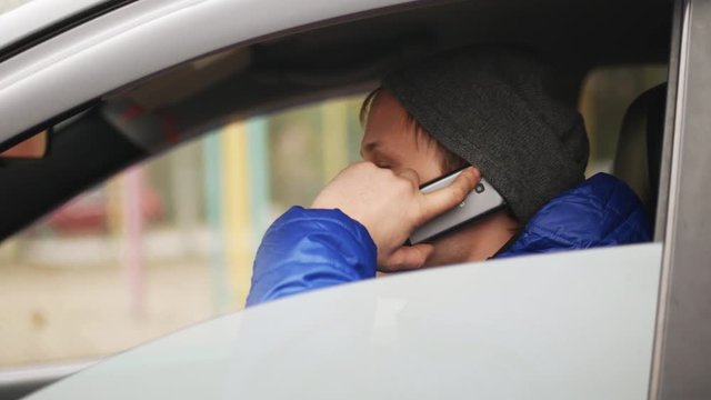 Man talking on the mobile phone in parked car. View through the windshield.