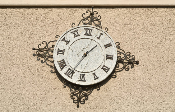 Vintage clock with Roman numbers - showing twenty-five to two - on stone wall
