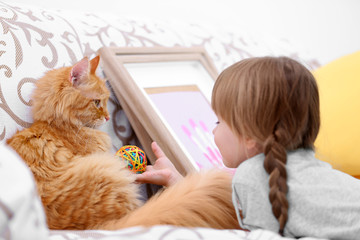 Fototapeta na wymiar Cute little girl and red cat on sofa, closeup