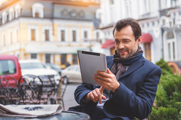 Cheerful man entertaining with gadget in cafeteria