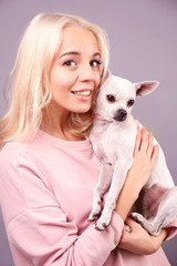 Beautiful girl holding cute dog on grey background