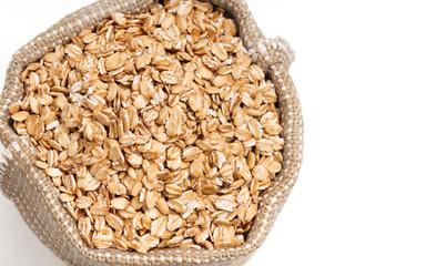Burlap sack filled with oat flakes on white background. Healthy food. Top view, copy space, high resolution product