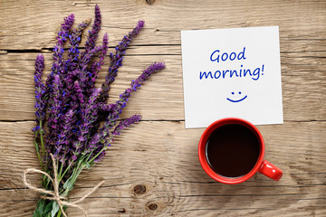 Flowers of salvia, coffee cup and paper with Good morning text on wooden table top view