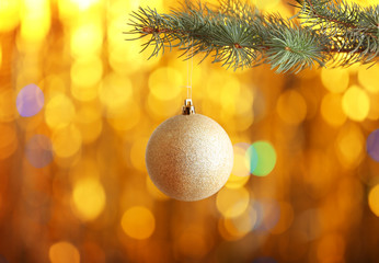 Christmas ball hanging on fir tree branch on blurred golden lights background