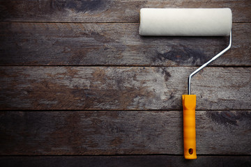 Painting roller on wooden background, top view
