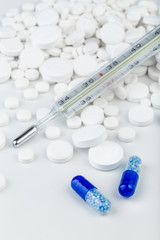 Bunch of white tablets with blue pills and thermometer.