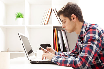 young man with cellphone and laptop at home