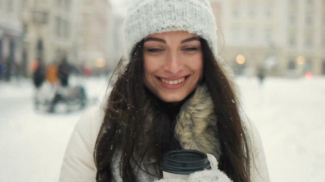 happiness, winter holidays, christmas, beverages and people concept - Cheerful gorgeous brunette in winter fashion holding disposable cup on urban background