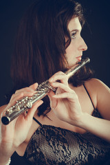 Woman playing transverse flute on black.