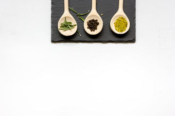 various spices in wooden spoons on white background top view