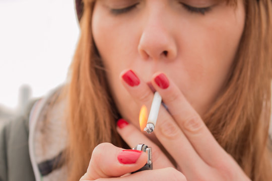 smoking young woman lighting cigarette outdoors close up. concept of nicotine addiction by teenagers