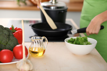 Fresh vegetables, salad and vegetable oil at the background of  woman is cooking by the stove in the kitchen