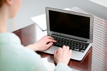 Business woman hands in a green blouse sitting at the desk in the office and typing on the laptop .