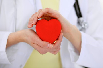 Female doctor with stethoscope holding heart.  Patients couple sitting in the background