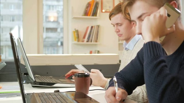 Young man working in the office of the laptops on the project. One is calling on the phone to the customer and records the answers. The concept of teamwork