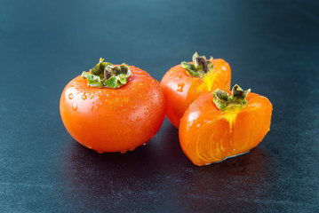 ripe persimmons with water drops on black