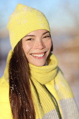 Winter season girl smiling outside in snow. Portrait of Asian woman happy outdoors with healthy smile on sunny wintertime day wearing yellow hat and scarf outerwear fashion outfit.