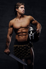 Portrait of shirtless muscular male holds silver gladiator helme