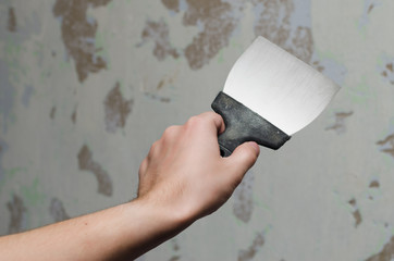 Trowel in man's hand on a background of ragged wall. Tool for getting rid of the wallpaper. 