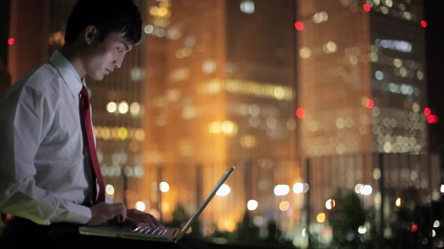 MS TU Businessman using laptop with cityscape in background at night / Beijing, China