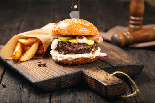 Burger with fries on wooden board on dark wooden table